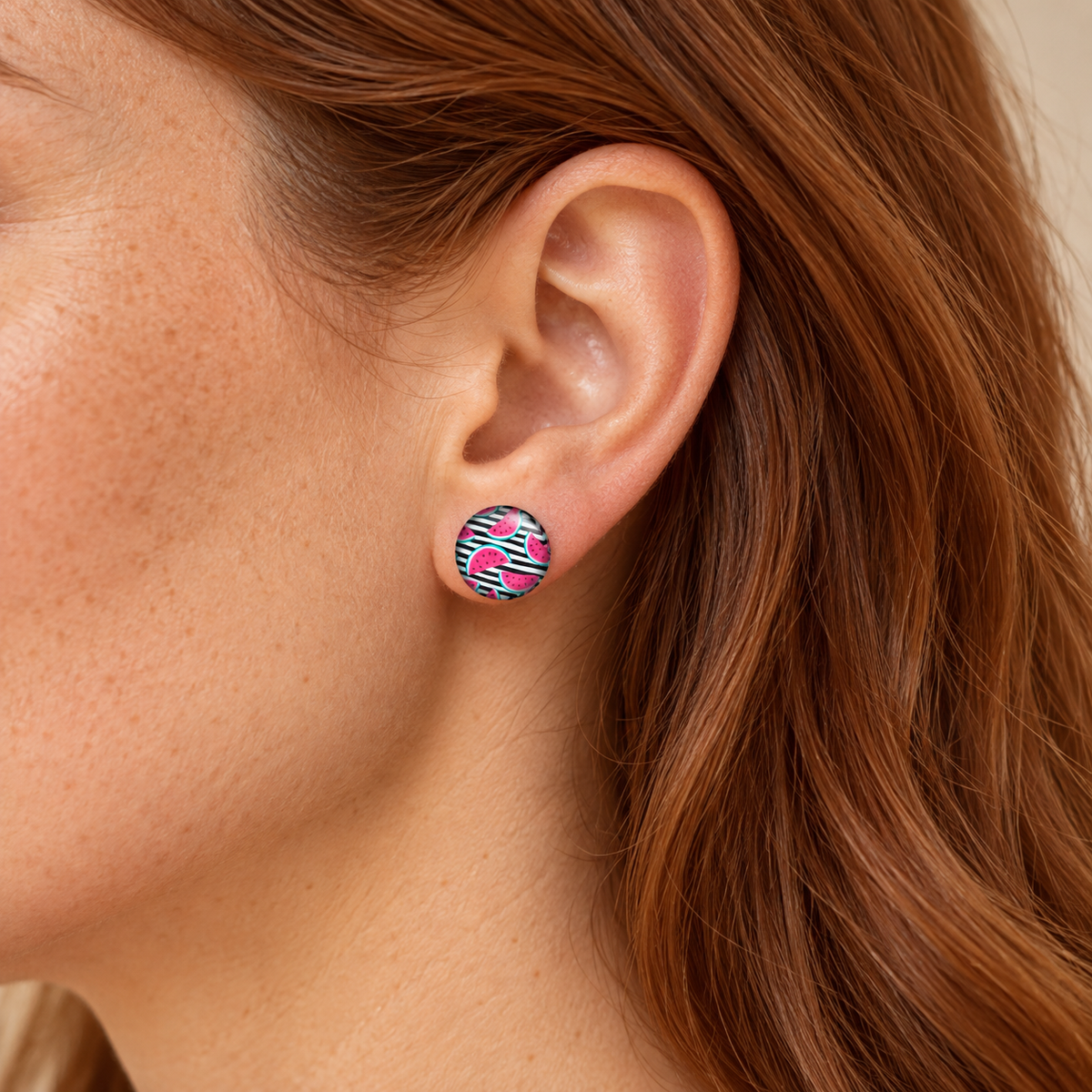 12-mm-Ohrstecker mit pinken Melonen auf schwarz-weißen Streifen am Ohr einer Frau mit roten Haaren.