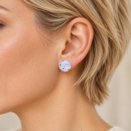 Weiße 12-mm-Ohrstecker mit lila und pinken Schmetterlingen am Ohr einer Frau mit blonden kurzen Haaren.