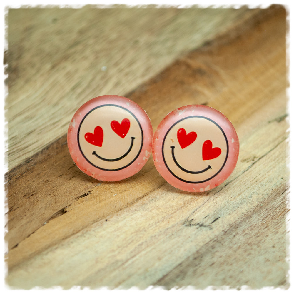 Jackelina Ohrstecker mit lächelndem Smiley und roten Herzaugen auf Rosa, als Paar auf Holz fotografiert
